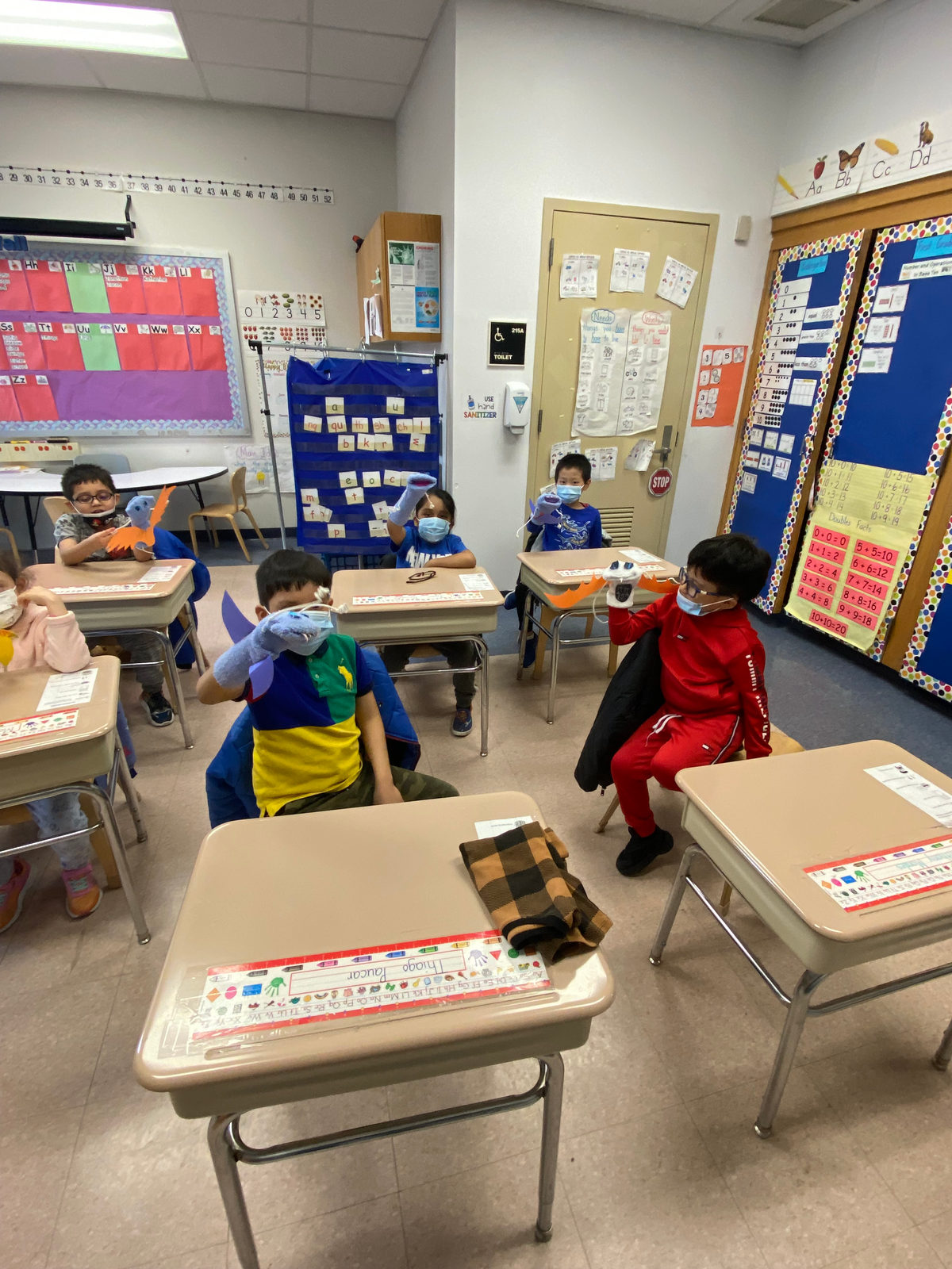 Students at their desks practice with their puppets