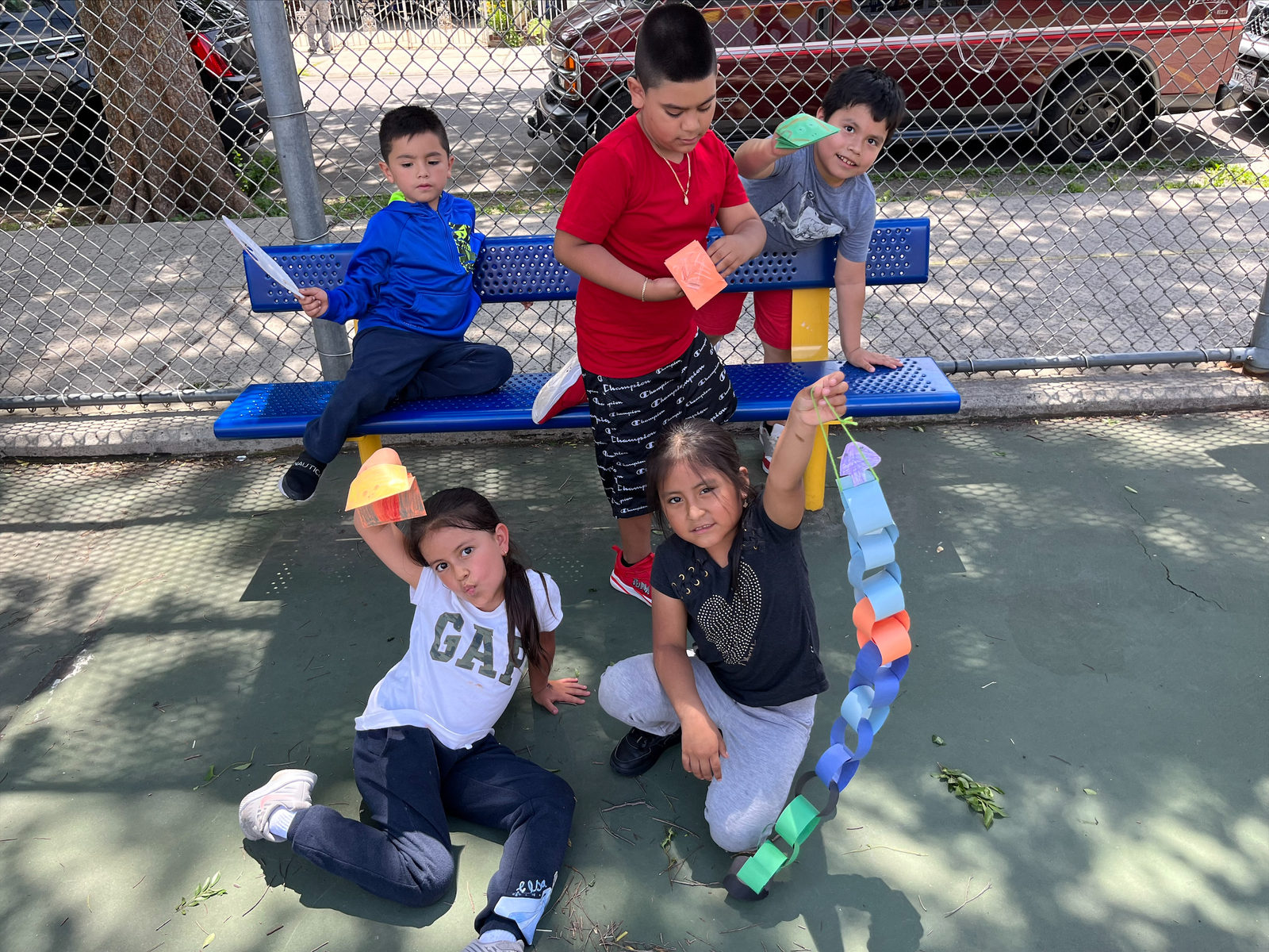 Students pose by a bench with their colorful paper chain puppets