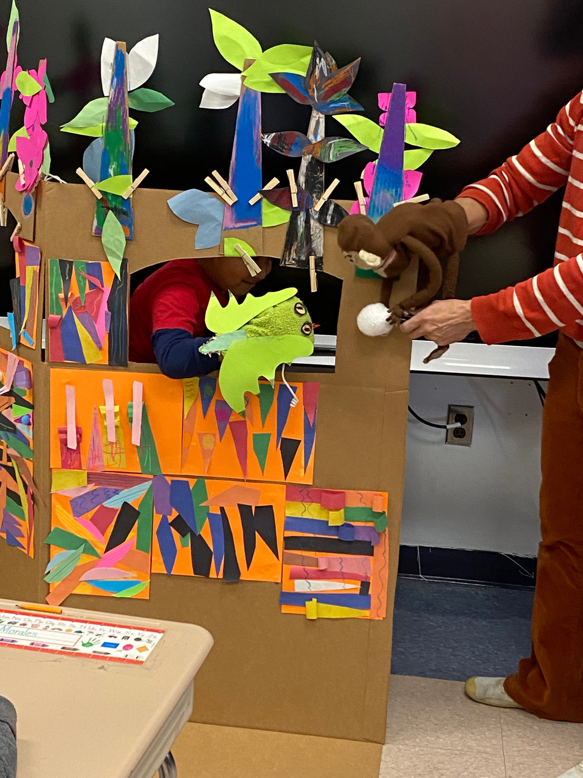 Students put on a puppet show from behind the colorful cardboard puppet stage their class built