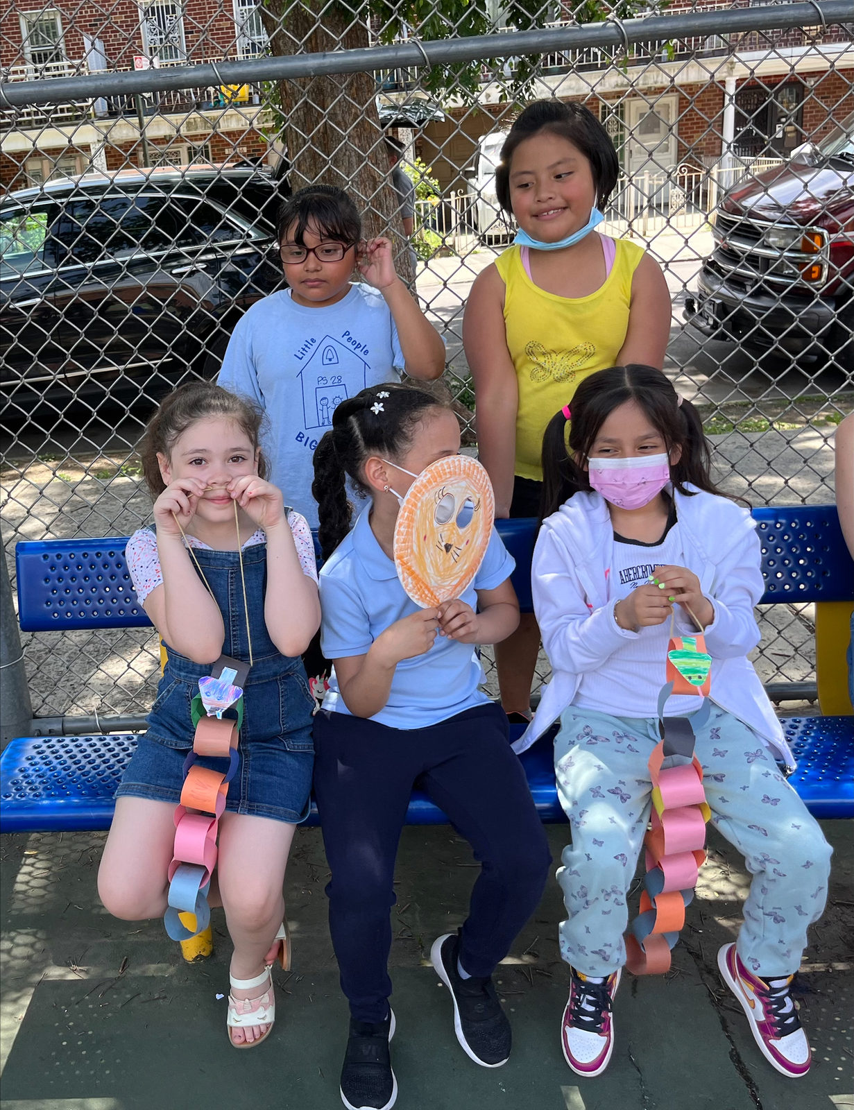 Students sit on a bench holding their paper puppets and paper chains