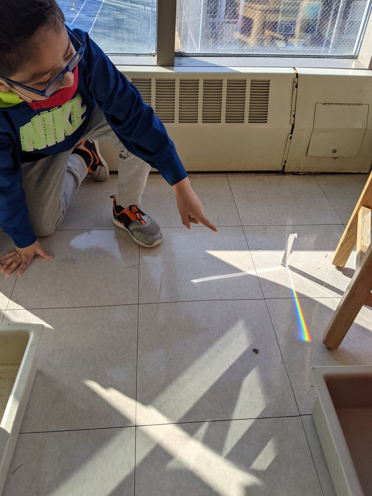 Student pointing at a rainbow made by a prism on the floor