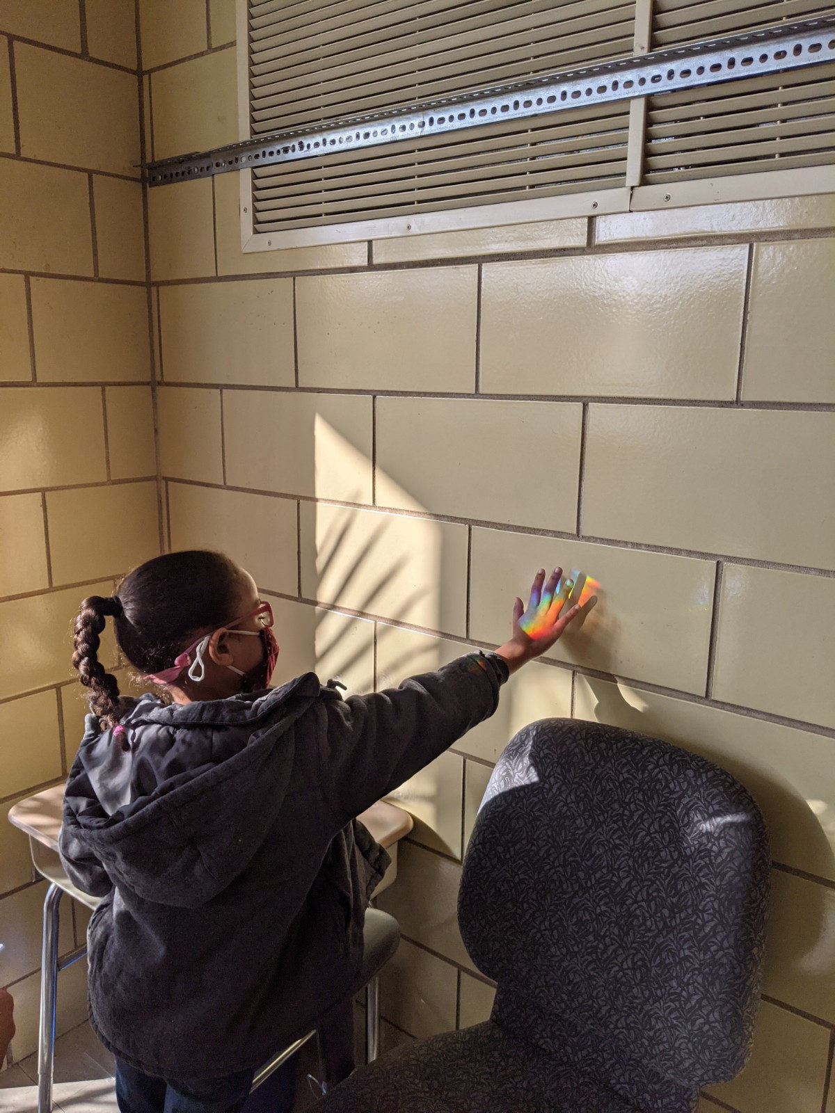 Student holding her hand in a patch of rainbow light on the wall