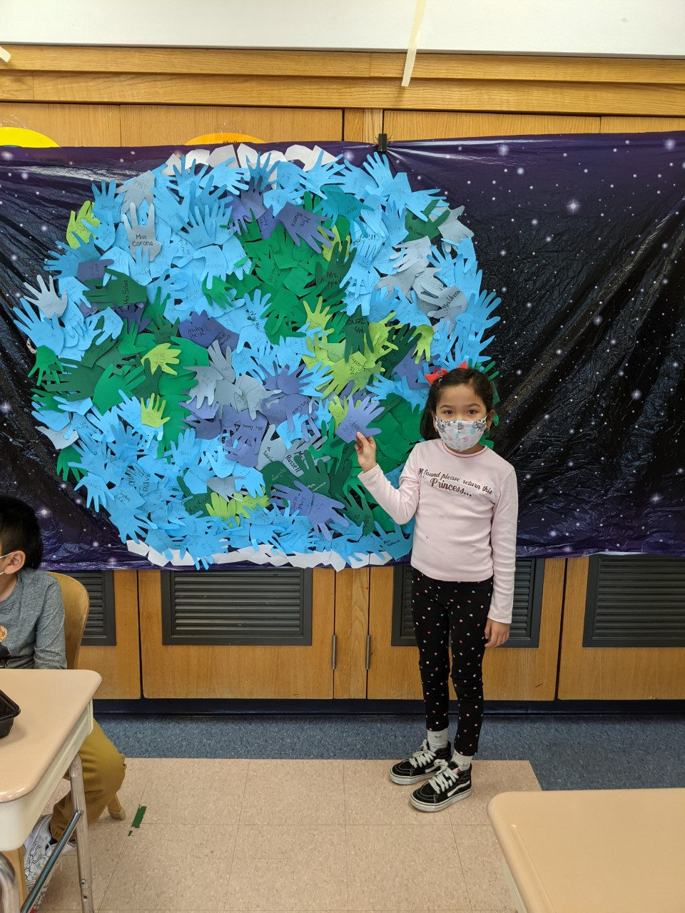 Student beside a hand-print Earth mural