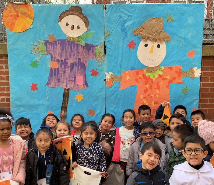Class smiling in front of a scarecrow mural at the Fall Festival