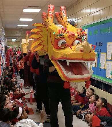 Paper dragon parading down the hallway as students in red watch